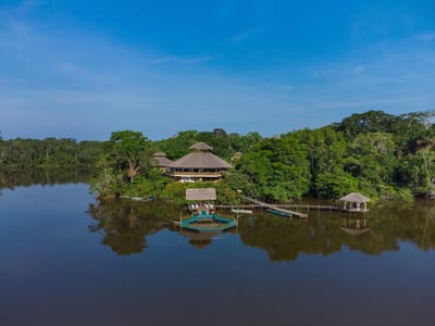 A thatched lodge pavilion reflected on a calm Amazon lagoon, Ecuador.