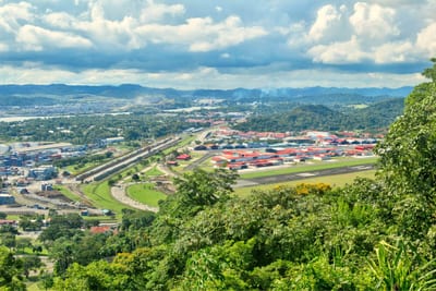 A panoramic view from the green slopes of Ancon Hill overlooking red-roofed buildings, roads, and rolling hills in Panama City, Panama.