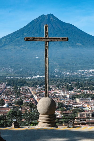 The stone cross at the Cerro de la Cruz viewpoint overlooking the rooftops of Antigua with the conical Volcán de Agua beyond, Guatemala.