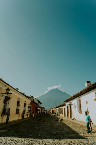 A cobblestone street in Antigua Guatemala leads toward a volcano on the horizon.