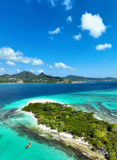 An aerial view of a small green islet ringed by white sand and turquoise reef off the coast of Antigua in the Caribbean.