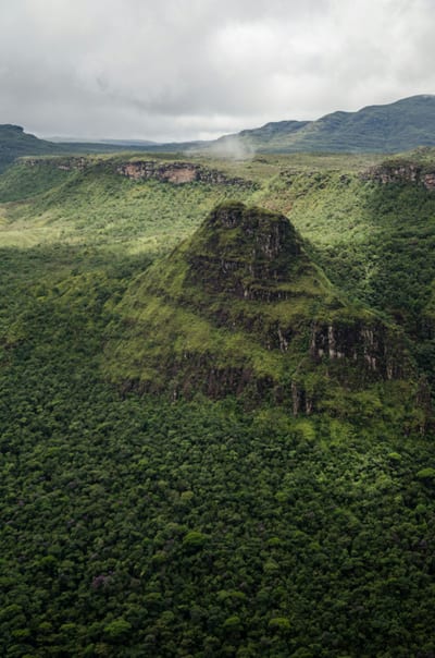 A lush green forested mountain rising from dense Atlantic-forest canopy under a misty sky in the Brazilian highlands.