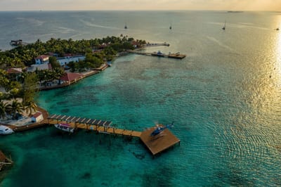 A wooden pier reaches over calm turquoise Caribbean water from a private island at golden hour, Belize.