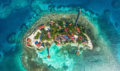 A private island encircled by turquoise reef in the Belize Caribbean, seen from the air.