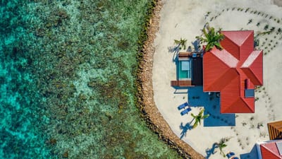 An aerial view of a thatched cabana on a sandbar ringed by turquoise reef off the coast of Belize.