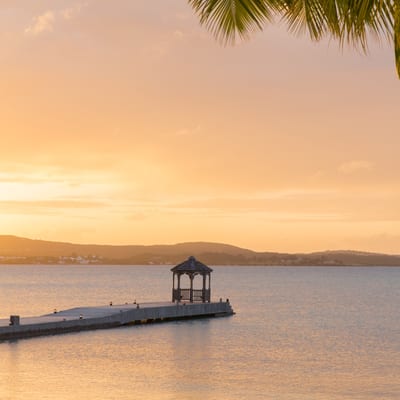 A sailboat on calm Caribbean water at golden hour.