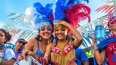 Two smiling carnival dancers in sequined costumes and large feathered headdresses at a street festival
