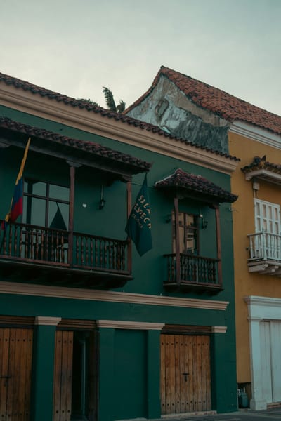 A colorful green-and-yellow colonial building with wooden balconies, tiled roofs and the Colombian flag in the walled old town of Cartagena, Colombia.