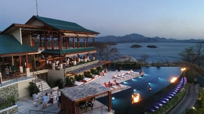 Guests by the clifftop infinity pool lit with flaming torches at dusk, beside the green-roofed lodge above the Pacific bay at Casa Chameleon, Las Catalinas, Costa Rica