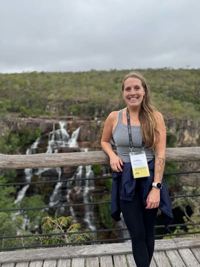 A smiling traveler stands at a wooden overlook railing above a multi-tier waterfall in the cerrado plateau of Chapada dos Veadeiros National Park, Brazil.