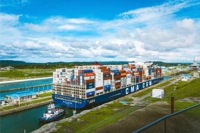 A CMA CGM container ship stacked high with cargo transiting the Panama Canal locks with a tugboat alongside