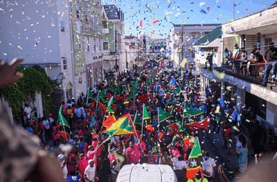 Confetti-filled street carnival parade with crowds and flags along a colonial street in the Caribbean
