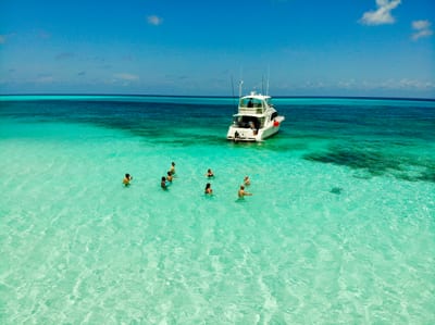 Snorkelers wading on a shallow turquoise sandbar beside a boat in the crystal-clear Caribbean water off Cozumel, Mexico.