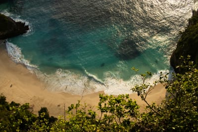 An aerial view of a turquoise cove with waves breaking on a golden-sand beach at Fernando de Noronha, Brazil.