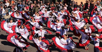Folkloric dancers in red-and-white costumes performing in formation at a street parade