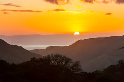 Vivid orange sunset over rolling forested mountains with a distant gulf in Costa Rica