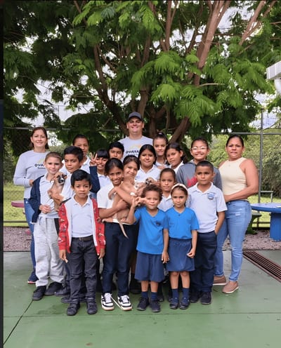 Local schoolchildren in uniforms pose with sanctuary staff under a large tree during an education visit at Guayabo Animal Rescue &amp; Sanctuary, Costa Rica.
