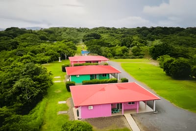 Aerial view of pink and green cabins with red roofs surrounded by lush forest and hills at Guayabo Animal Rescue &amp; Sanctuary in Guanacaste, Costa Rica.