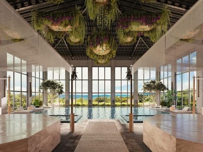 Indoor spa pool at Hacienda AltaGracia under a vaulted ceiling of cascading greenery and purple flowers, with loungers and floor-to-ceiling windows onto the Pérez Zeledón mountains, Costa Rica
