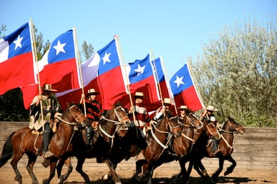 Huasos on horseback carrying Chilean flags in formation during Fiestas Patrias