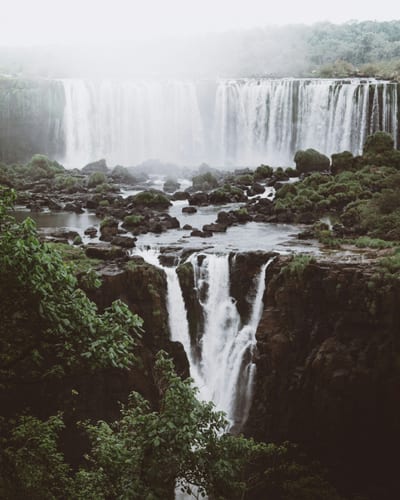 A misty daytime aerial of the Iguazú Falls cascading over the cliff into the jungle gorge below, Brazil.