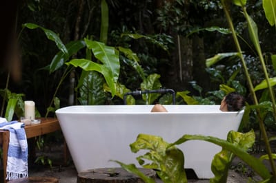 A traveler soaks in a freestanding outdoor bathtub surrounded by lush tropical rainforest foliage at Isla Palenque private island, Panama.