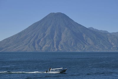 A small boat crosses Lake Atitlán beneath the cone of a volcano, Guatemala.