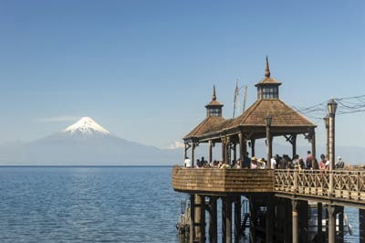 A wooden pier reaches into a lake in Chile's Lake District beneath a snow-dusted volcano.