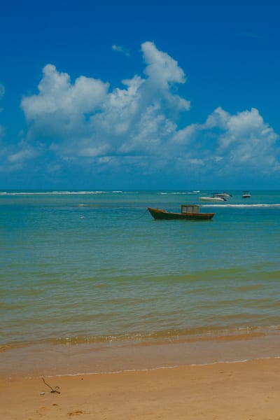 A wooden fishing boat anchored in calm turquoise shallows off a sandy beach on the Bahia coast, Brazil.