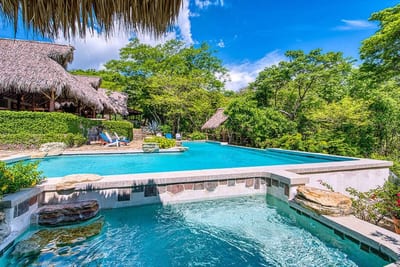A tiered swimming pool with a stone-edged spa, thatched-roof palapas, and surrounding tropical forest at Morgan's Rock eco-lodge near San Juan del Sur, Nicaragua
