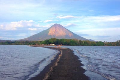 The symmetrical cone of Concepción volcano rises beyond a narrow sandbar reaching into Lake Nicaragua on Ometepe Island, with visitors walking along the spit, Nicaragua.