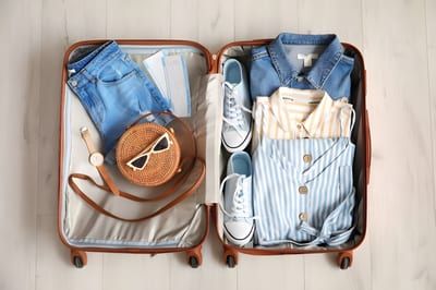 Overhead view of an open suitcase neatly packed with summer clothes, sneakers, a straw bag and travel documents