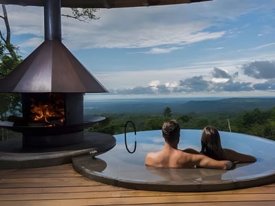 Couple in a private villa plunge pool beside a suspended wood-burning fireplace, overlooking the rainforest at Origins Lodge in Bijagua, Costa Rica