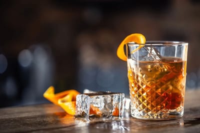 A rum cocktail served over a large ice cube in a cut-crystal glass with an orange-peel garnish on a wooden bar, evoking Panama's nightlife.