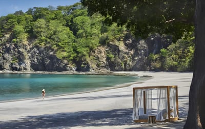 Secluded crescent beach with turquoise water and a curtained four-poster beach cabana under a shade tree on the Papagayo Peninsula in Guanacaste, Costa Rica