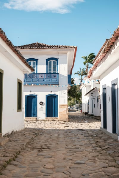 A cobblestone street lined with whitewashed colonial houses with blue doors and trim in the historic center of Paraty, Rio de Janeiro state, Brazil.