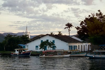 A blue and white wooden boat floats on calm water in front of whitewashed colonial houses at Paraty, Rio de Janeiro state, Brazil.