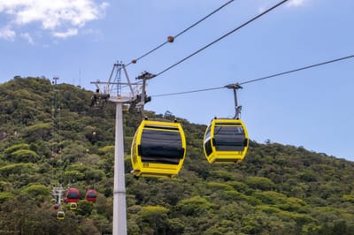 Yellow Metrocable gondola cars glide over forested green hills on the cable-car line to Parque Arví above Medellín, Colombia.