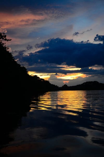 A wide Amazon river at dusk in the Peruvian rainforest.