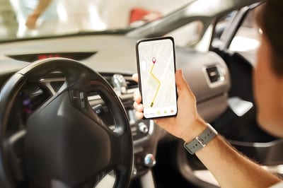 Driver holding a smartphone showing a GPS navigation map with a plotted route inside a car