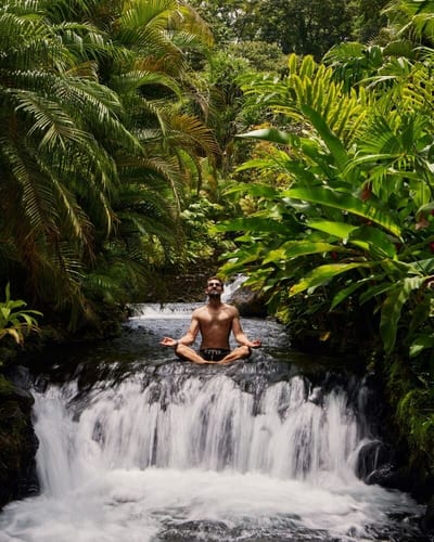 A man meditating atop a jungle waterfall surrounded by lush rainforest, Costa Rica