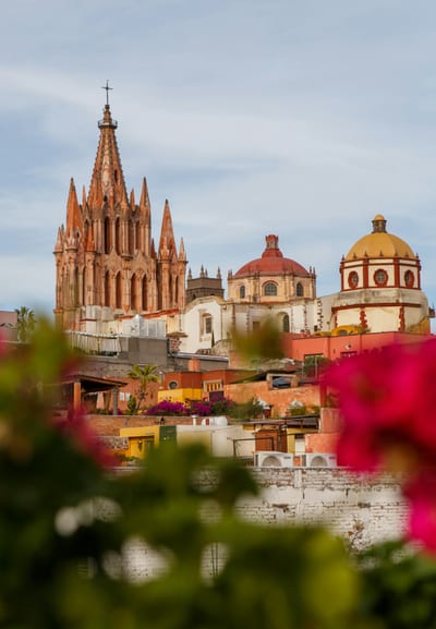 A rooftop view over San Miguel de Allende with the pink Parroquia spire and church domes rising behind bougainvillea, Mexico.