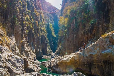 Two travelers scrambling over boulders deep inside the towering limestone walls of Somoto Canyon, with green river water below, in northern Nicaragua