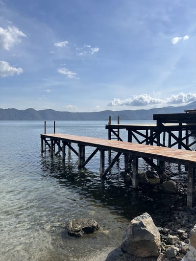 A long wooden pier extends over the calm water of Lake Suchitlan near the colonial town of Suchitoto, El Salvador.