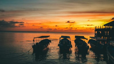 Silhouetted travelers on a boat at sunset over the Caribbean Sea near Roatán, Honduras.