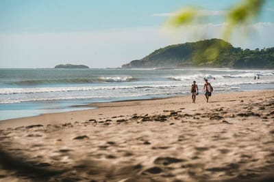 Surfers carrying their boards across a wide, empty Pacific surf beach on Nicaragua's southwest coast.