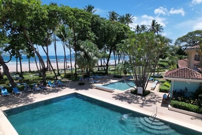 Beachfront swimming pools with blue loungers among palms by day, steps from Tamarindo Beach and the Pacific, at Tamarindo Diria Beach Resort in Guanacaste, Costa Rica