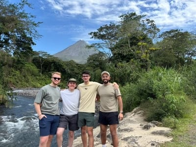 Four travelers posing by a river with the cone of the Arenal Volcano behind them, Costa Rica