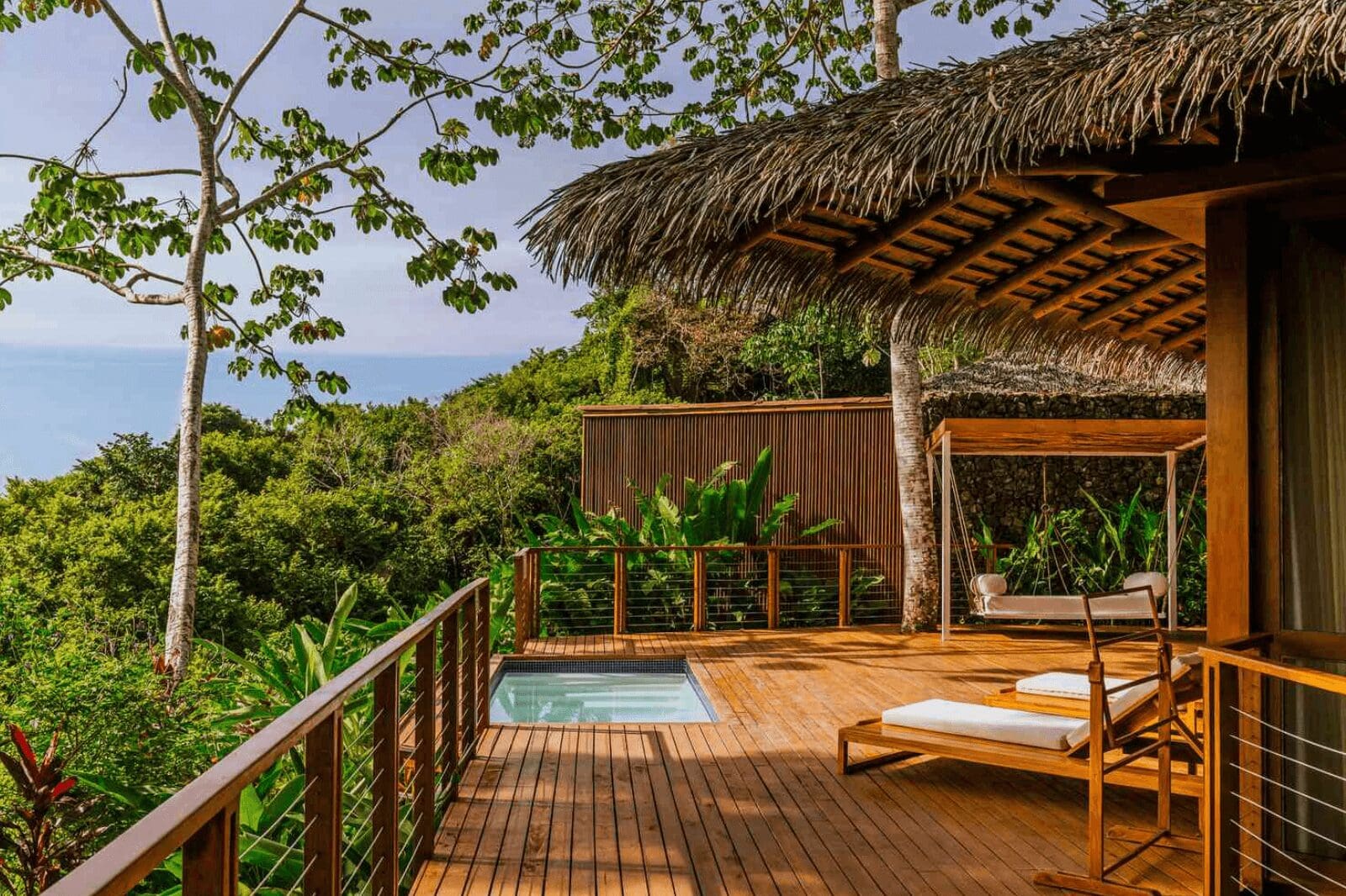 Aesthetic wooden eco-lodge surrounded by lush trees and bushes, with a serene view overlooking the ocean.