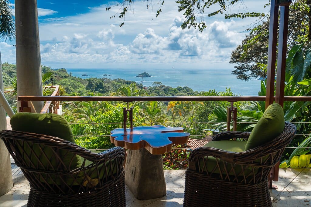 Ocean-view lounge area at a rainforest hotel in Manuel Antonio, Costa Rica, with wicker chairs overlooking the Pacific coastline and tropical jungle.